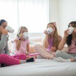slumber party: 4 young women sitting on a bed, all of them drinking from mugs